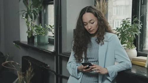 Smiling Woman Using Smartphone Indoors By Window
