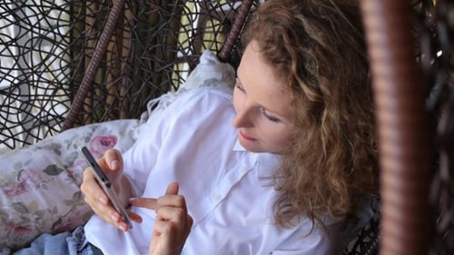Woman Using Smartphone in Hanging Chair Indoors