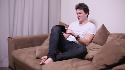 Young Adult on Couch Using Tablet, Headphones