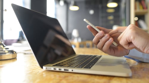 Adult Using Phone Near Open Laptop in Office