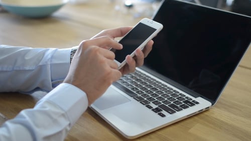 Person Using Smartphone Near Laptop