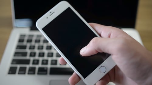 Hand Uses Smartphone With Laptop in Background