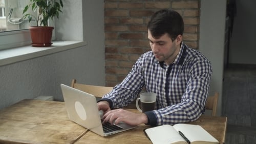 Ein Mann in einem karierten Hemd starrt auf den Monitor und trinkt einen Schluck Kaffee.