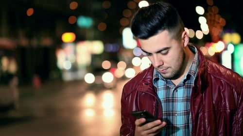 Young Man Uses Phone on City Street at Night