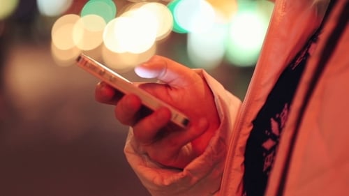 Hand Using Cellphone at Night with Bokeh Lights
