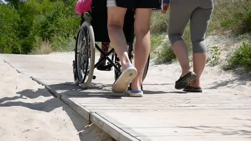 Family Leisure. Young Woman and Man with There Disabled Mother in Wheelchair Walking in the Park