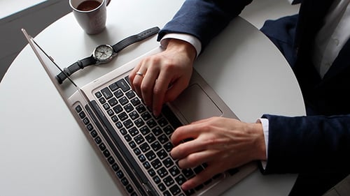 Man Types on Laptop at Desk with Coffee
