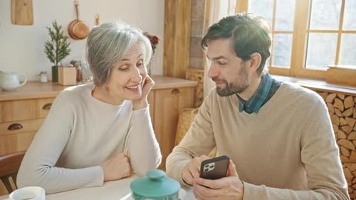 Senior Woman and Adult Son Look at Phone