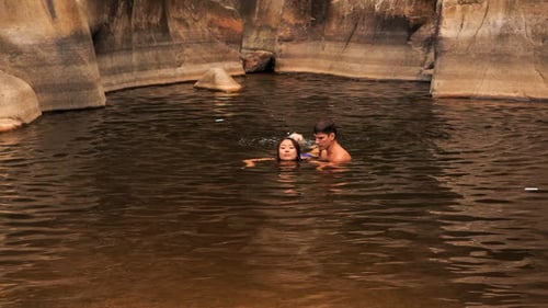 Guy Carries in Arms Girl Helping Swim in Lake Created by Stream