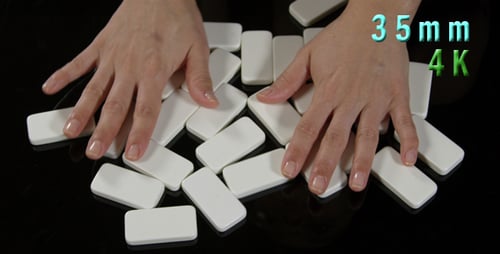 Hands Arranging White Dominoes on a Black Surface