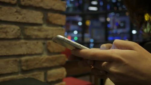 Woman Using Mobile Phone at Night in Urban Cafe