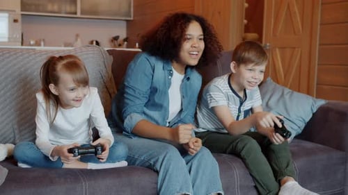Joyful Young Babysitter Cheering Kids Playing Video Game Having Fun in Apartment