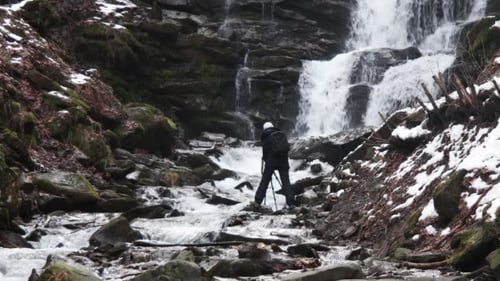 Waterfall Flows as Adventurer Explores Snowy Terrain