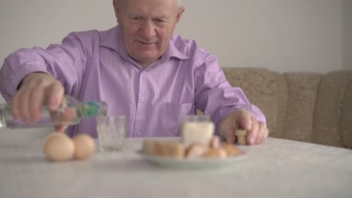 Senior Man en chemise bleue s'assoit à la table et boit de la vodka