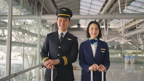 Portrait of attractive Asian airliner pilot and air hostess standing in airport terminal smiling.