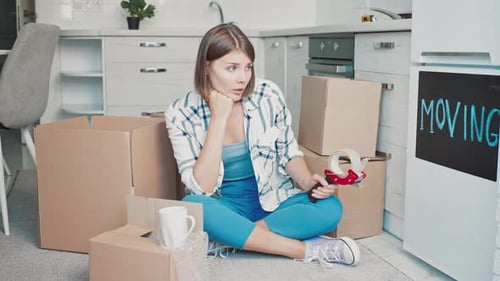 Woman sits overwhelmed by moving boxes
