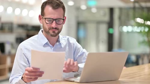 Businessman Working on Laptop and Documents in Office