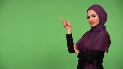 A Young Beautiful Muslim Woman Points at a Bulletpoint Text and Looks at the Camera Green Screen