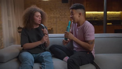Couple singing playfully with kitchen utensils on sofa