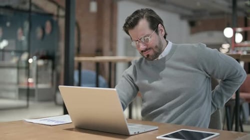 Young Man Having Back Pain While Using Laptop in Office