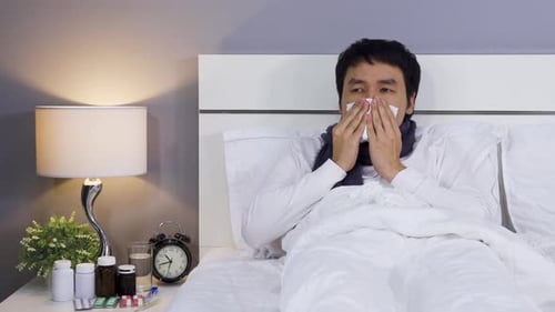 homme malade éternuant dans un mouchoir couché dans son lit