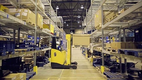 Forklift Operator Loading Container on Metal Rack in Warehouse