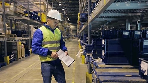 Arbeiter im Lager geht an Regalen entlang und überprüft Behälter in Regalen