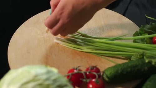 Closeup of a Young Girl Cuts Fresh Green Onions on a Wooden Board
