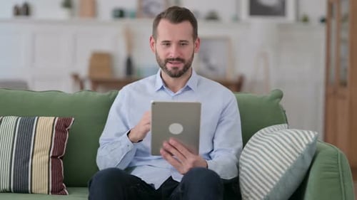 Bearded Man Celebrates Using Tablet on Sofa