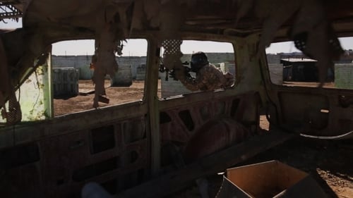Paintballer avec fusil automatique passe devant une voiture brûlée