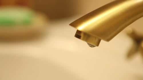 Water Droplets Falling from a Gold Faucet