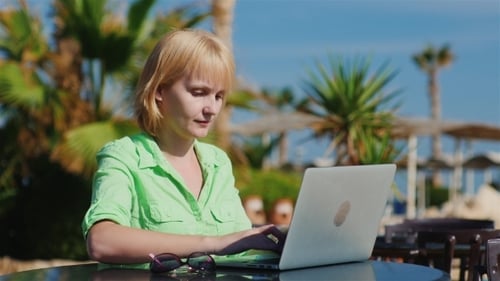 Woman Tourist Is Typing On a Laptop On a Background Of Mediterranean Recreational Areas