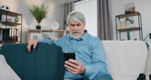 Senior Man Using Smartphone on Couch Indoors