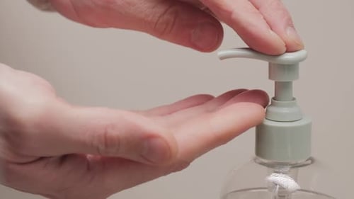 Nahaufnahme männlicher Hände, die mit flüssiger transparenter Seife auf einen Spender drücken, um sich die Hände auf einem weißen