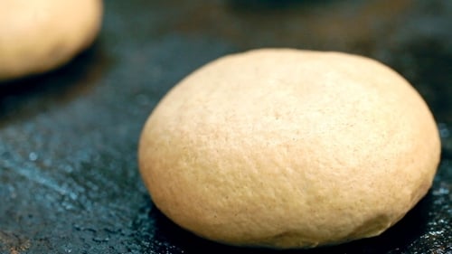 Ein Bäcker schmiert ein Brötchen mit Öl.