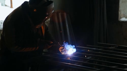 Masked Metalworker Welding Metal Bars in Dark Workshop