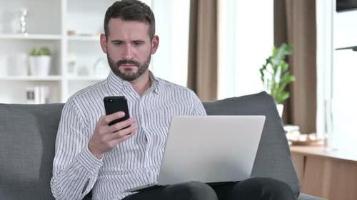 Man Working on Laptop and Using Phone at Home