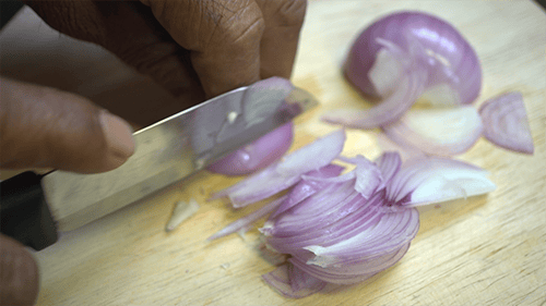 Hand Slicing a Red Onion on Board