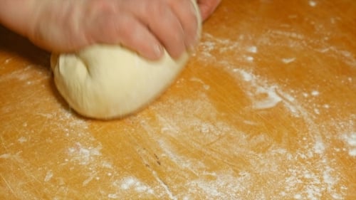 Hands Kneading Dough on Floury Wooden Surface