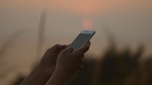 Smartphone in hands at scenic sunrise or sunset
