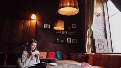 Young Woman Drinking Coffee And Using Tablet Computer In a Coffee Shop