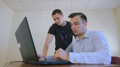 Two Young Businessmen Discussing a Startup With a Laptop At Office
