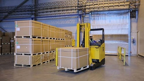 Mann auf Gabelstapler transportiert Fracht von einem Lager zum anderen