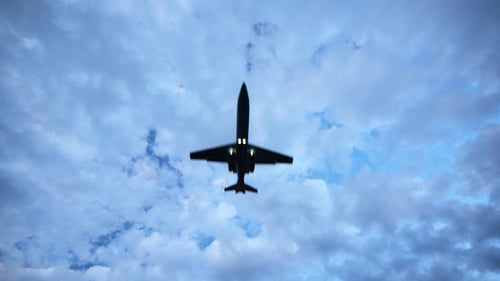 Airplane Flies Across Fluffy Clouds on Sunny Day