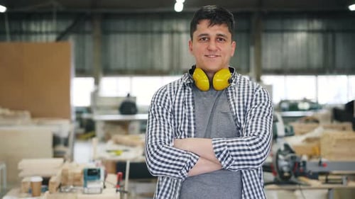 Porträt eines attraktiven jungen Schreiners, der mit verschränkten Armen in der Werkstatt steht