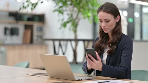 Young Woman Working at Desk With Laptop and Phone