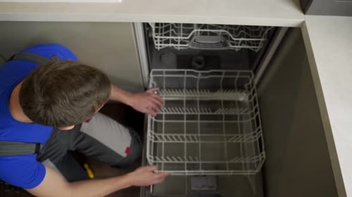 Repairman Checks Operating State of Dishwasher in Kitchen