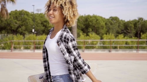 Stylish Young Adult with Skateboard Walks Outdoors