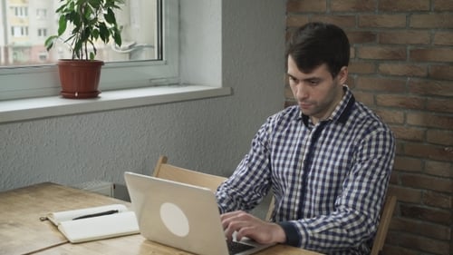 Young Adult Typing on Laptop at Wooden Table