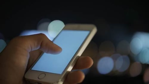 Hand Using Smartphone at Night with City Lights